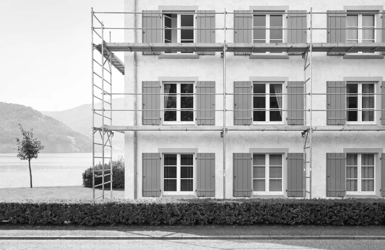 Frisch gestrichene Fassade eines Mehrfamilienhauses mit Gerüst, grünen Fensterläden und Blick auf den See.